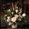 A festive centerpiece with white tulips, roses, silver accents, and pinecones. Designed