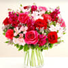 This arrangement features red and pink roses, red carnations, and pink alstroemeria