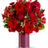 This arrangement features a vibrant mix of red flowers, including roses, gerbera