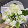 Hand-tied bouquet of white roses, lilies, orchids, and hydrangea wrapped in white mesh and paper