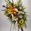 A vast array of sunflowers, roses and greenery on a stand. 
Colors