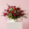 Styled arrangement in predominantly red blooms with hues of burgundy and fuschia.