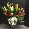 White lilies, red roses, lisianthus, pink tulips in a tall vase.