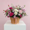 A sweet basket arrangement with pink and white blooms, fresh greenery, and