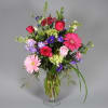 An explosion of brilliant colors, featuring gerbera daisies, roses and larkspur. The