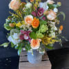 Large vase style arrangement in a specialized container featuring roses, ranunculus, helleborus