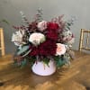 Roses and carnations with alstroemeria and assorted greens in a pink container.