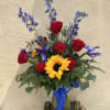 Red roses, blue delphinium, sunflower, iris &amp; mixed seasonal blooms create this