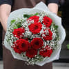 A bouquet of twelve red roses with decorative green leaves and Baby