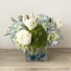 Blue hydrangeas with white ranunculus and tulips in a cube vase with