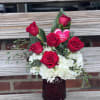 A arrangement including six red roses, hydrangea and greenery in a red