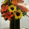 Arrangement composed of orange lilies, yellow sunflowers, red carnations, with hints of