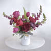 Jewel toned premium blooms professionally arranged in a white ceramic vase and