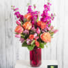 A pleated, magenta vase is filled with brilliant orange and pink garden