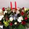 A festive holiday centerpiece featuring classic red roses, elegant white lilies, textured