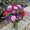 A bold colored arrangement of roses, daisies, carnations, and filler flowers arranged