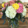 Pretty pink, yellow ranunculus mixed with hydrangeas, roses, hyacinthus, and seasonal greens.