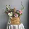 A rustic wicker basket brimming with pink roses, white blooms, and seasonal