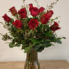 A dozen long stemmed red roses with coordinating seasonal greenery and accent