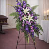 A dignified purple and white floral arrangement displayed on a stand, conveying