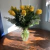 one dozen yellow roses in a vase with filler and greens