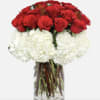Red roses above white hydrangeas in a clear glass vase