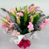 A lush wrapped bouquet of pink lilies, carnations, and greenery, tied with