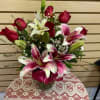 Mixed arrangement with red roses, stargazer lilies, and wax flowers in a