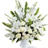 A serene standing arrangement of white lilies, roses, snapdragons, and lush greenery.