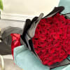 An opulent hand-tied bouquet featuring dozens of rich red roses, wrapped in