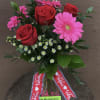 Gerbera and roses arranged in a clear vase with greens and filler.