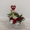 A romantic floral arrangement featuring red roses, red carnations, white lilies, baby&rsquo;s