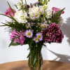 This classic arrangement features purple and white seasonal flowers, hand-designed inside a