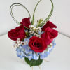 5 red roses nestled in a hydrangea with a lily grass heart