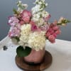 A sleek cylinder vase with pink leaf rap overflowing with lush white