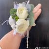 This wrist corsage features white ranunculus, eucalyptus leaves, rhinestones and colored stones.