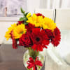 Red and yellow flowers in a clear glass vase with a red ribbon