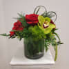 red roses and an orchid in a low vase with greenery shaped