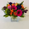 a bright mixed arrangement in a vase. includes: Gerber Daisies, Roses, Spray