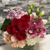 A lush compact arrangement using red roses, hydrangeas, stock and cymbidium orchids.