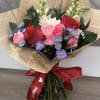 Red and pink roses with seasonal accents and greenery, hand-wrapped in decorative