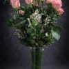 One dozen pink roses arranged in a tall clear vase.