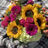 cylinder vase filled with sunflowers. orange gerbera daisys, hot pink roses and