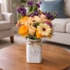A warm toned floral arrangement featuring gerbera daisies, roses, and delicate wildflowers