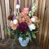 Soft peaches, pinks, and lavender blooms arranged in a frosted white vase