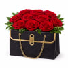 A chic black handbag-style keepsake container filled with lush red roses and