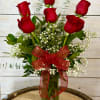 This features a half dozen roses arranged in a vase with filler