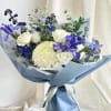 A front-facing, asymmetric bouquet with blue and white flowers, greenery, wrapped in