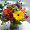 It has gerbera daisy, blue delphinium, red roses, orange Asiatic lily and