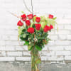 Red roses arranged in a tall glass vase with branches and greenery